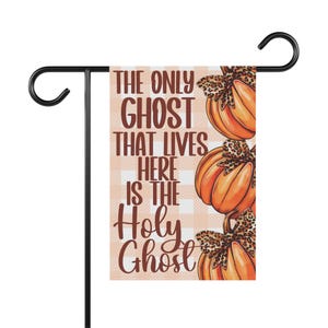 May include: A fall-themed garden flag with a checkered background and the text "The only ghost that lives here is the Holy Ghost". Three pumpkins with leopard print bows are stacked on top of each other.