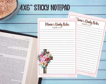 May include: Pink 4x6 inch sticky notepad with lined pages. The notepad features the text "Marie's Daily Notes" and "Isaiah 41:10" in a decorative font. A floral cross design is on the bottom left corner. The notepad is on a light blue surface.
