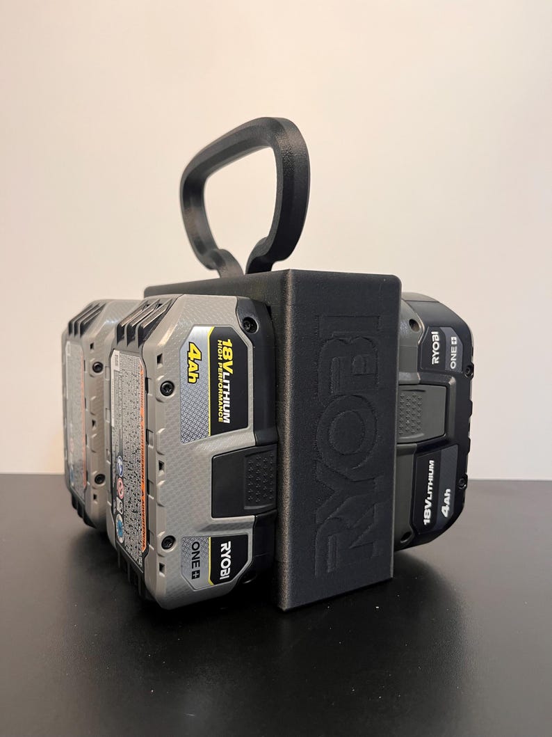 May include: A black Ryobi battery holder with a handle, holding four 18V Lithium 4Ah batteries. The Ryobi logo is visible on the side of the holder. The batteries are gray and black.