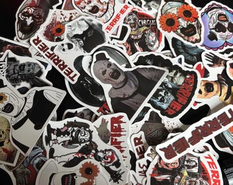 Puede incluir: Una colección de pegatinas de temática de terror con varios personajes y diseños. Las pegatinas muestran imágenes de payasos, calaveras y otras figuras espeluznantes, con la palabra "TERRIFIER" destacada en varias. Las pegatinas son de varios tamaños y formas.
