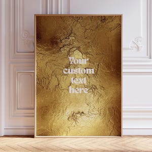 Peut inclure: Une affiche encadrée avec un motif en feuille d'or texturé. L'œuvre d'art présente le texte "Your custom text here" dans une police blanche et élégante. L'impression est exposée dans une pièce avec des boiseries blanches et un parquet.