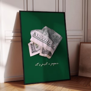 May include: A framed art print with a crumpled hundred-dollar bill on a dark green background. The text "it's just a paper" is written in a cursive font at the bottom. The frame is black, creating a modern aesthetic.