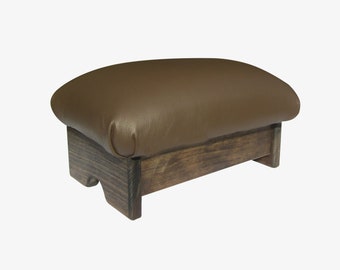 May include: A brown leather-covered footstool with a wooden base. The footstool has a rounded top and a rectangular base.