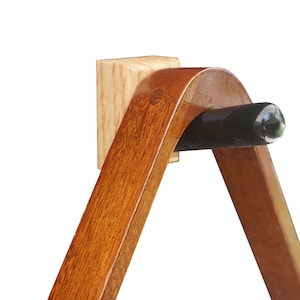 May include: A wooden billiard triangle rack with a black rubber tip on the corner. The rack is mounted to a wall with a wooden block.