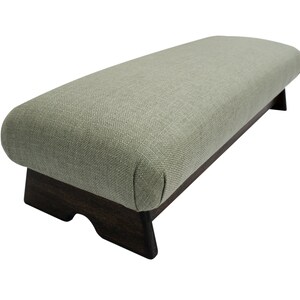 May include: A light green upholstered footstool with a dark wood base. The footstool has a rounded top and a rectangular base.
