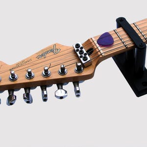May include: A brown electric guitar with chrome tuning pegs and a black guitar stand. The guitar has the word "Fender" printed on the body and "Stratocaster" printed on the headstock.