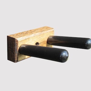 May include: A wooden wall mount with two black metal hooks for hanging guitars. The hooks have rubber tips to protect the guitar finish.