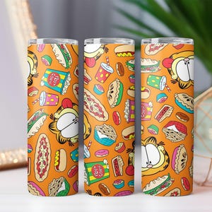 Puede incluir: Tres vasos naranjas con un patrón repetido de Garfield el gato, rebanadas de pizza, palomitas de maíz, donas y otros alimentos. Los vasos son cilíndricos y parecen estar hechos de metal o un material similar.