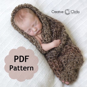 Könnte beinhalten: Ein braunes gehäkeltes Baby-Wickeltuch mit einem PDF-Muster zum Häkeln. Das Tuch ist hellbraun mit einem dunkelbraunen Muster. Das Tuch ist um ein schlafendes Baby gewickelt.