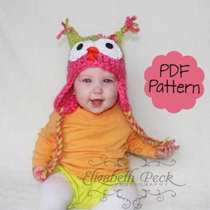 Puede incluir: Un gorro de ganchillo rosa y verde en forma de búho con trenzas largas. El gorro tiene ojos de fieltro blanco y un pico naranja brillante. El gorro lo lleva un niño con una camisa naranja brillante.