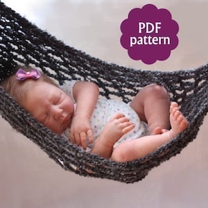 Può includere: Un'amaca in crochet grigia con un bambolotto che dorme al suo interno. L'amaca è appesa in alto nell'immagine. Il bambolotto indossa un body bianco con pois rosa e ha un fiocco viola nei capelli. Il testo "PDF pattern" è in una nuvola viola nell'angolo in alto a destra dell'immagine.