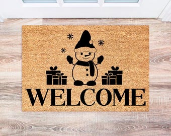 May include: A brown coir doormat with a black snowman design and the word "WELCOME" in black lettering.
