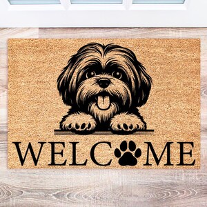 May include: A rectangular doormat with a light brown background and a black illustration of a dog with its tongue out. The word "WELCOME" is printed in black, with a paw print replacing the "O".