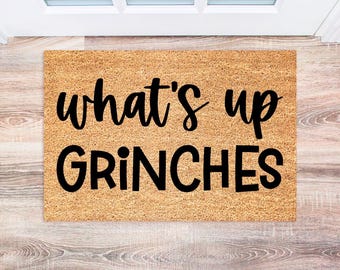 May include: A brown coir doormat with the text "what's up GRINCHES" in black lettering.