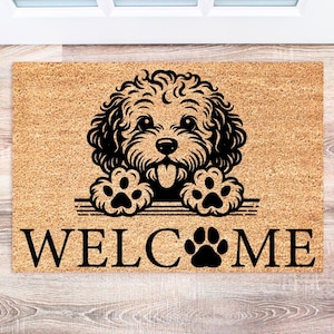 May include: A rectangular doormat with a light brown background and a black illustration of a dog with its tongue out. The word "WELCOME" is printed in black, with a paw print replacing the "O".