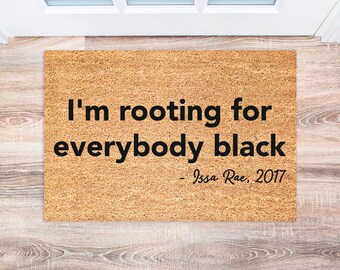 Może przedstawiać: Brązowa mata kokosowa z nadrukiem "I'm rooting for everybody black - Issa Rae, 2017" w kolorze czarnym.
