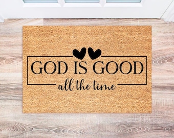 May include: A brown coir doormat with the text "GOD IS GOOD - all the time" in black lettering. Two black hearts are above the text.