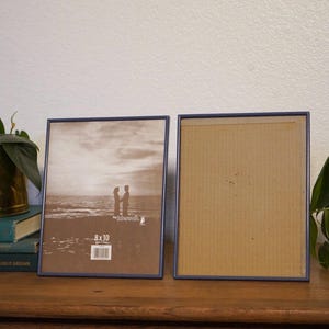May include: Two rectangular picture frames with navy blue borders. One frame contains a black and white photo of a couple on a beach. The other frame is empty. The frames are 8 x 10 inches.