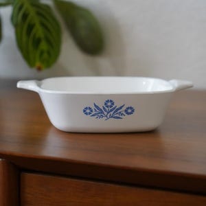 May include: White rectangular baking dish with blue floral design. The dish has two handles on the sides.