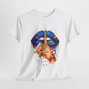 May include: White t-shirt with a graphic design. It features blue lips decorated with puzzle pieces and the words "DON'T JUDGE WHAT YOU DON'T UNDERSTAND." A hand with a finger to the lips and an autism awareness ribbon are also shown.