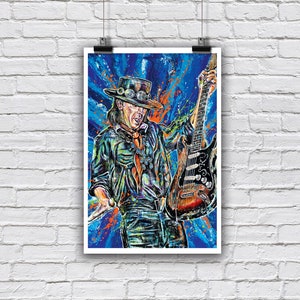 May include: A vibrant, colorful art print depicting a musician wearing a wide-brimmed hat with goggles, a dark shirt, and a neck scarf, playing a sunburst electric guitar. The background features dynamic blue and orange paint splatter effects.
