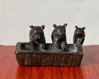 May include: A dark brown metal rectangular trough-shaped container featuring three small pig figures attached to the rim. The exterior of the container has a textured, basket-weave pattern, and the interior is smooth with a metallic finish.