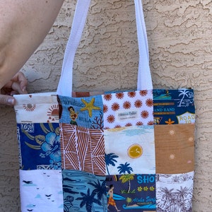 May include: A white canvas tote bag with patchwork fabric featuring a variety of tropical and beach-themed designs. The bag has white straps and is made by Hibiscus Belles.