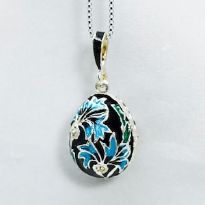 May include: A silver chain necklace with a black enamel egg pendant. The egg is decorated with blue and green floral designs and clear rhinestones.
