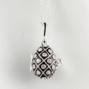 May include: Silver-tone teardrop pendant necklace. The pendant features a black enamel design with a diamond pattern and clear crystal accents. The pendant opens to reveal a small compartment. The necklace hangs on a delicate silver chain.