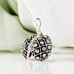 May include: A silver necklace with a pendant shaped like an egg. The egg pendant is black with a grid pattern and clear crystal accents. The pendant opens to reveal a red interior.