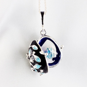 May include: A silver pendant necklace with a black and blue enamel locket. The locket is open and reveals a blue and white floral design inside.