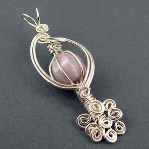 May include: A silver wire wrapped pendant featuring a light purple gemstone in a cage-like design. The pendant has a delicate, intricate design with multiple wire loops at the bottom.