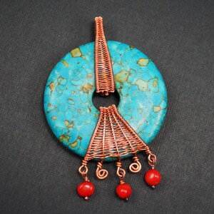 Könnte beinhalten: Türkis-Stein-Anhänger mit Kupferdraht-Design. Der Anhänger hat einen kreisförmigen Türkis-Stein mit einem Loch in der Mitte. Kupferdraht ist um den Stein gewebt und hängt mit drei roten Perlen herunter.