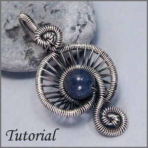 May include: A silver wire wrapped pendant featuring a blue gemstone in the center, surrounded by a circular wire design. The pendant is shaped like a treble clef.