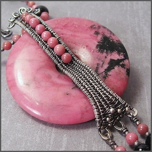 Peut inclure: Un pendentif en pierre précieuse rose et noire avec un enroulement de fil d'argent et des perles roses. Le pendentif est attaché à une chaîne en argent avec des perles roses.