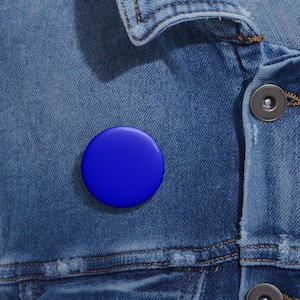 May include: A blue round button pin on a denim jacket.