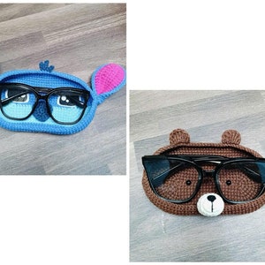 Op de afbeelding: Twee gebreide brillenhouders, een blauwe met roze oren en de andere bruin met bruine oren. Beide houders hebben zwarte brillen erin.