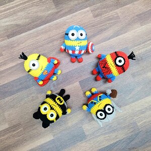 May include: Five handmade crochet Minion figures, each with unique superhero-themed designs. The figures are primarily yellow, blue, red, and black, with details like a Superman logo, Captain America shield, and Spider-Man web.