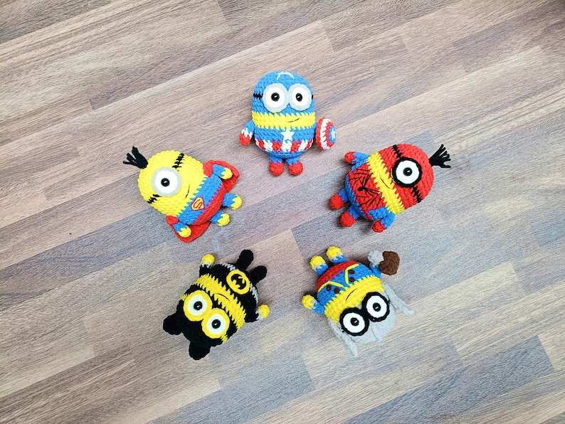 May include: Five handmade crochet Minion figures, each with unique superhero-themed designs. The figures are primarily yellow, blue, red, and black, with details like a Superman logo, Captain America shield, and Spider-Man web.