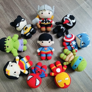 May include: A collection of crocheted superhero characters, including Spiderman, Iron Man, Hulk, Captain America, Thor, Batman, Superman, Venom, and a Teenage Mutant Ninja Turtle. The characters are all in different poses and have different expressions.