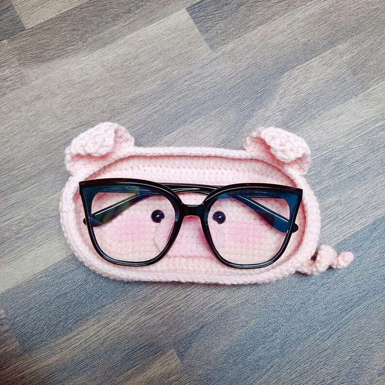 May include: A pink crocheted pig-shaped glasses case with black eyeglasses inside.