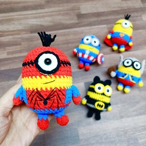 May include: A collection of handmade crochet Minion figures, each designed as a different superhero. The figures are primarily yellow, blue, red, and black, with details like a spider web and a Captain America shield.
