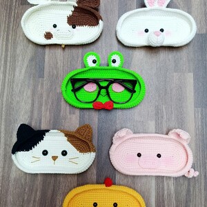 May include: Six crocheted animal-shaped trinket dishes. The dishes are shaped like a cow, rabbit, frog, cat, pig, and chick. Each dish has a cute face with embroidered details.