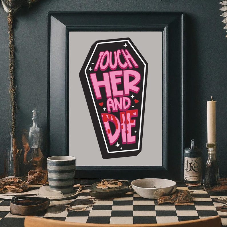 May include: A framed print featuring a coffin shape with the words "TOUCH HER AND DIE" in pink and white lettering. The artwork has a black border and is set against a gray background. The print is displayed on a checkered surface.
