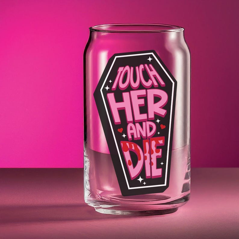 May include: A clear glass can-shaped drinking glass with the words "TOUCH HER AND DIE" in pink and white lettering inside a black coffin shape. The glass is set against a pink background.