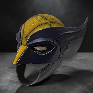 Puede incluir: Una m&aacute;scara estilo Wolverine, con una combinaci&oacute;n de colores amarillo y azul marino. La m&aacute;scara tiene una parte superior amarilla texturizada, detalles en azul oscuro y protuberancias en forma de ala en los lados. El &aacute;rea de los ojos tiene una cubierta de malla.