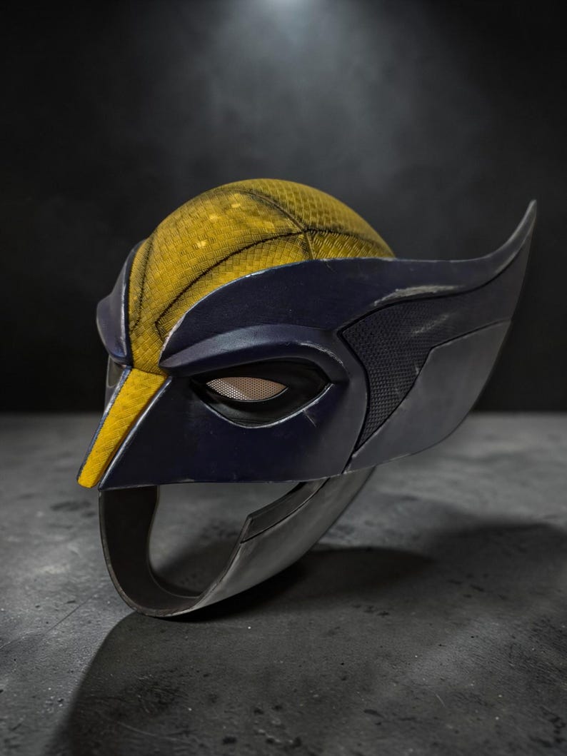Puede incluir: Una m&aacute;scara estilo Wolverine, con una combinaci&oacute;n de colores amarillo y azul marino. La m&aacute;scara tiene una parte superior amarilla texturizada, detalles en azul oscuro y protuberancias en forma de ala en los lados. El &aacute;rea de los ojos tiene una cubierta de malla.