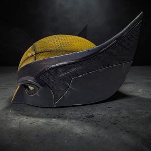 Puede incluir: Primer plano de una m&aacute;scara de Wolverine. La m&aacute;scara presenta una parte superior amarilla texturizada con detalles en negro y orejas puntiagudas. El &aacute;rea de los ojos es negra y la m&aacute;scara est&aacute; sobre un fondo oscuro.