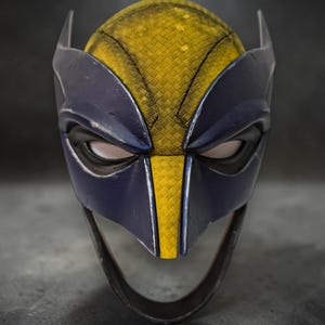 Puede incluir: Primer plano de una m&aacute;scara de Wolverine. La m&aacute;scara presenta una combinaci&oacute;n de colores amarillo y azul, con un patr&oacute;n texturizado en las &aacute;reas amarillas. Tiene orejas puntiagudas y aberturas para los ojos. Accesorio de disfraz de superh&eacute;roe.