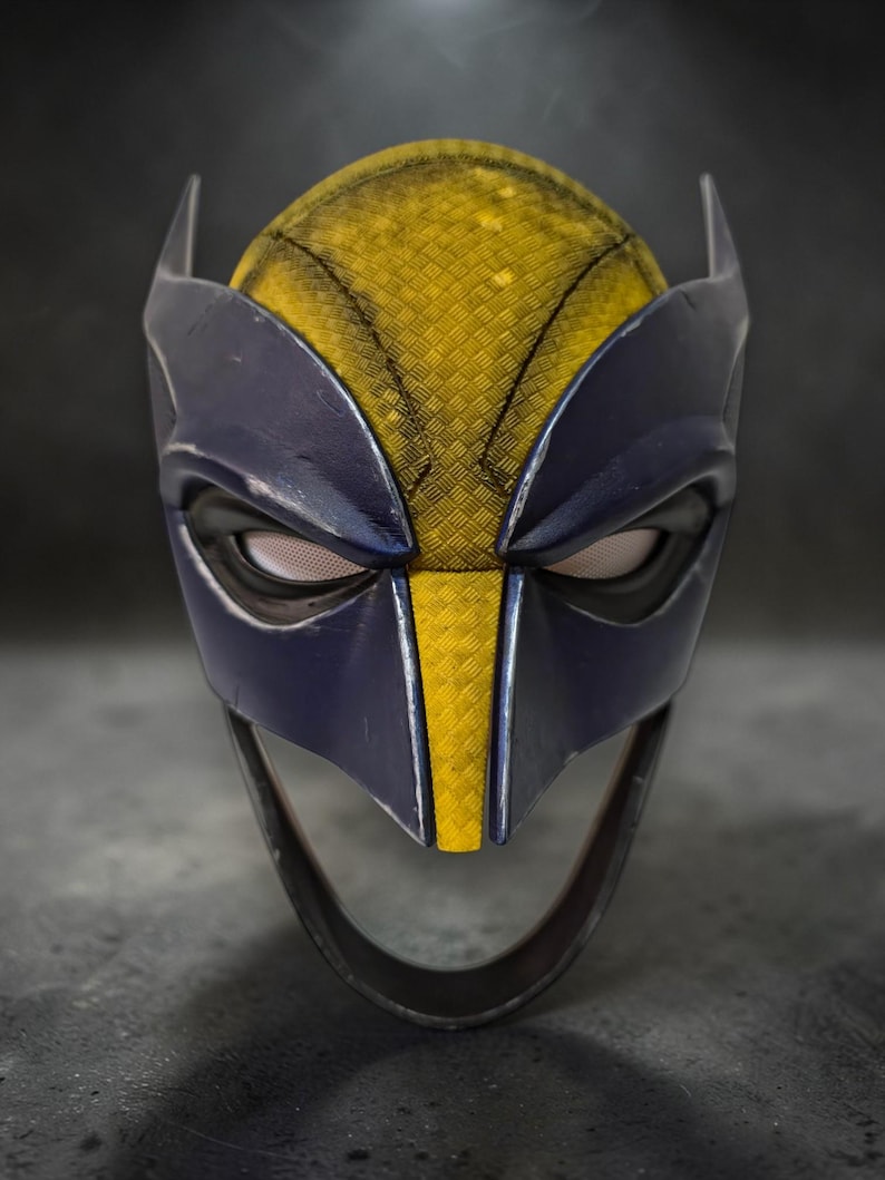 Puede incluir: Primer plano de una m&aacute;scara de Wolverine. La m&aacute;scara presenta una combinaci&oacute;n de colores amarillo y azul, con un patr&oacute;n texturizado en las &aacute;reas amarillas. Tiene orejas puntiagudas y aberturas para los ojos. Accesorio de disfraz de superh&eacute;roe.
